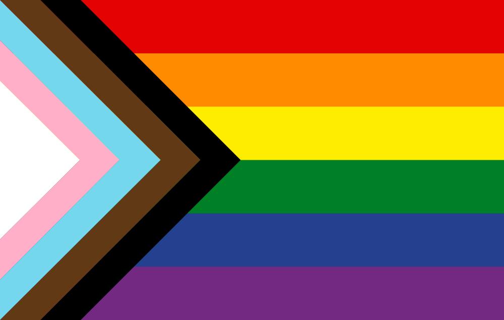 “Progress Pride Flag with six horizontal rainbow stripes and a left-pointing chevron in black, brown, light blue, pink, and white, symbolizing inclusion of LGBTQIA+ communities of color and transgender individuals.